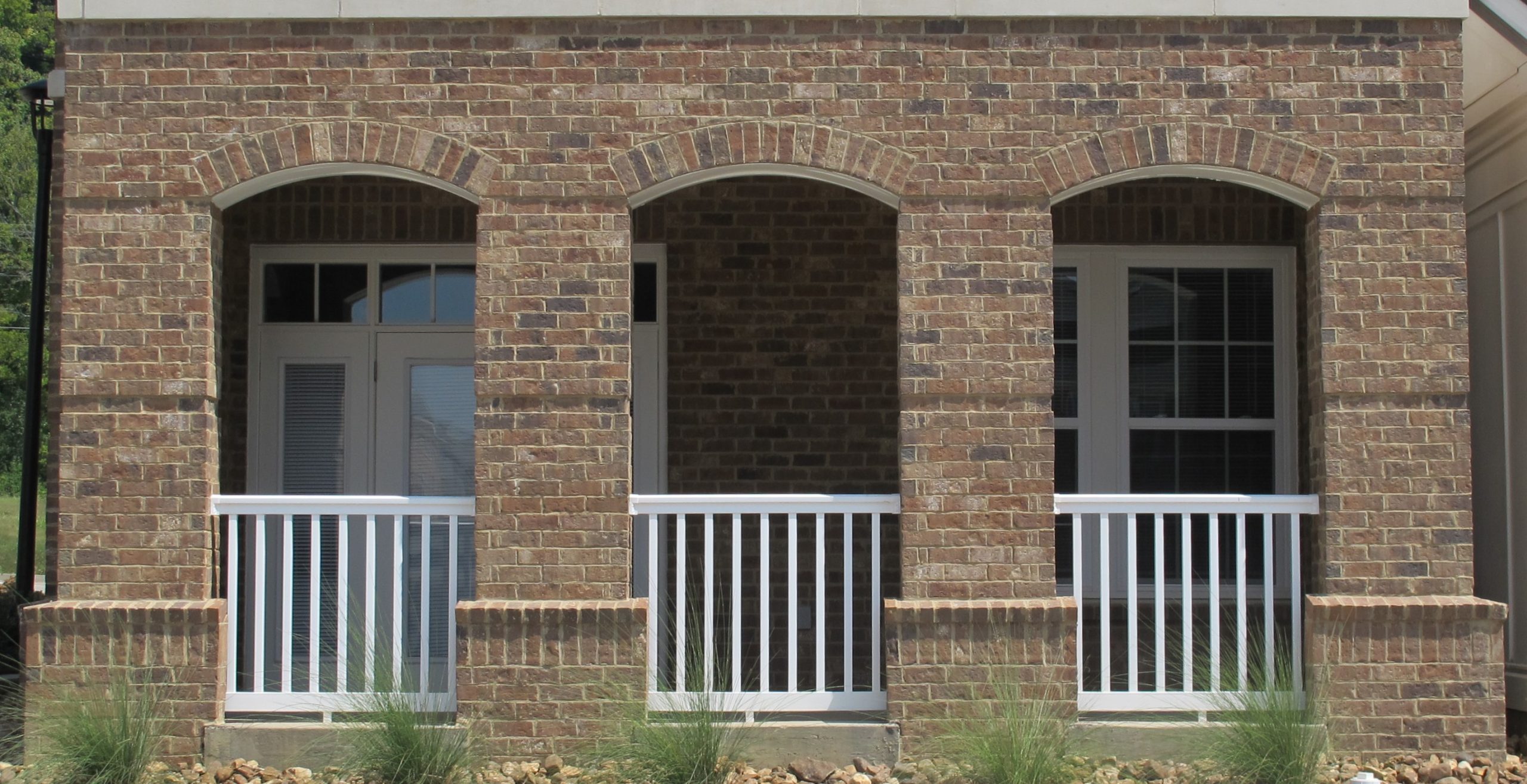  Red brick porch featuring round archways, white railing, and white trim that highlights the architectural details