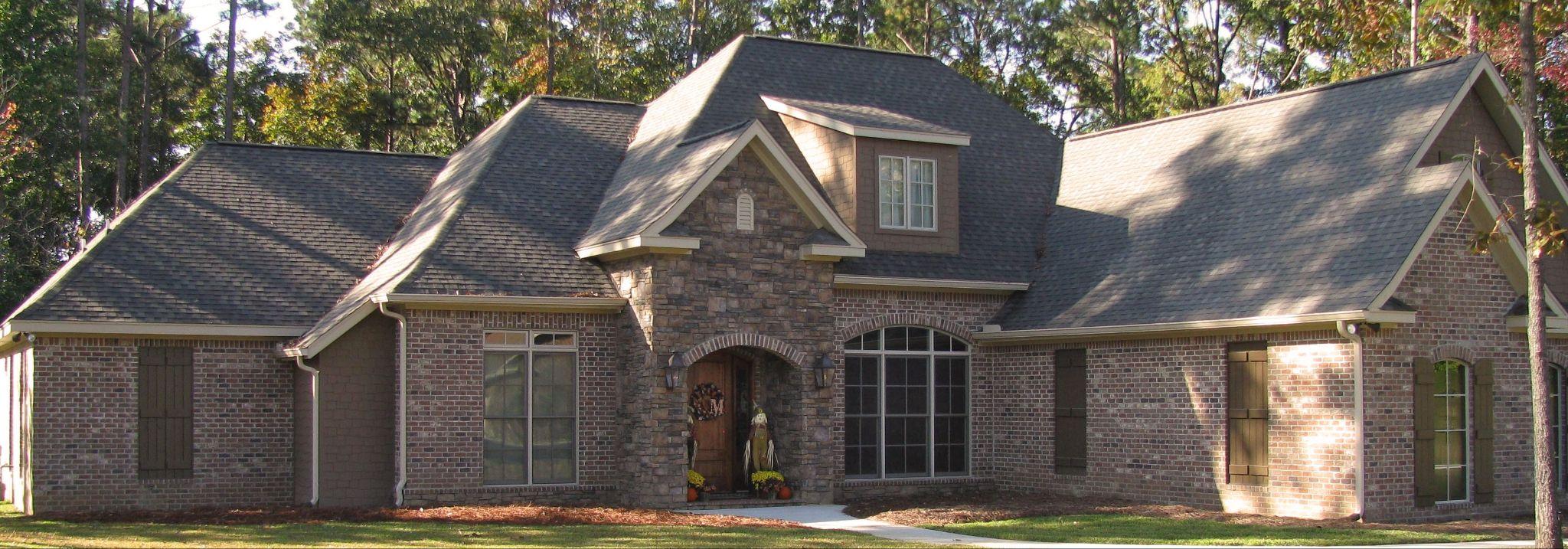 Front exterior of a sprawling Craftsman-style home featuring rich Forest Glen brick masonry, dark wooden accent shutters, and a prominent stone arched entryway with a wooden front door.